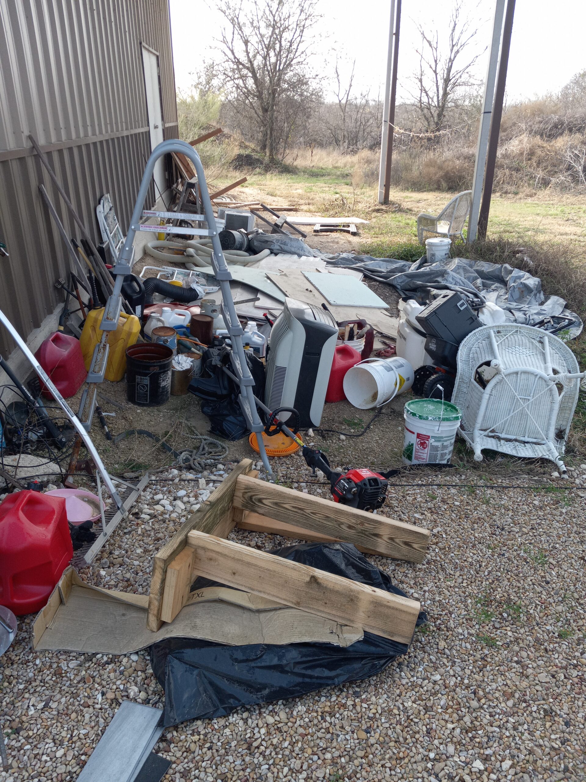 Messy outdoor storage area with tools, containers, and debris.