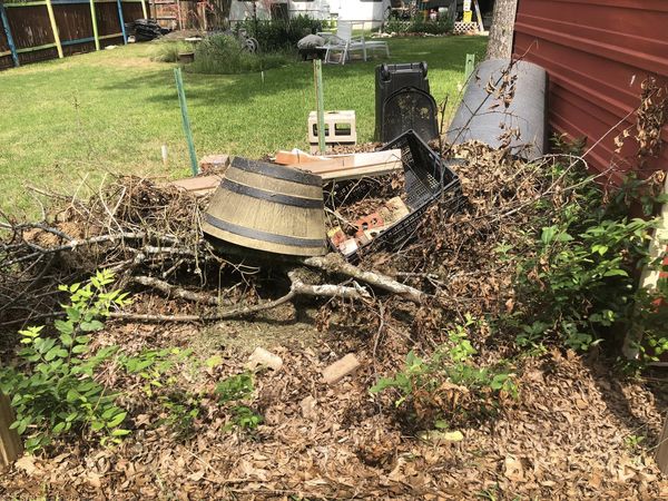 Backyard debris pile with discarded barrel, branches, and leaves.