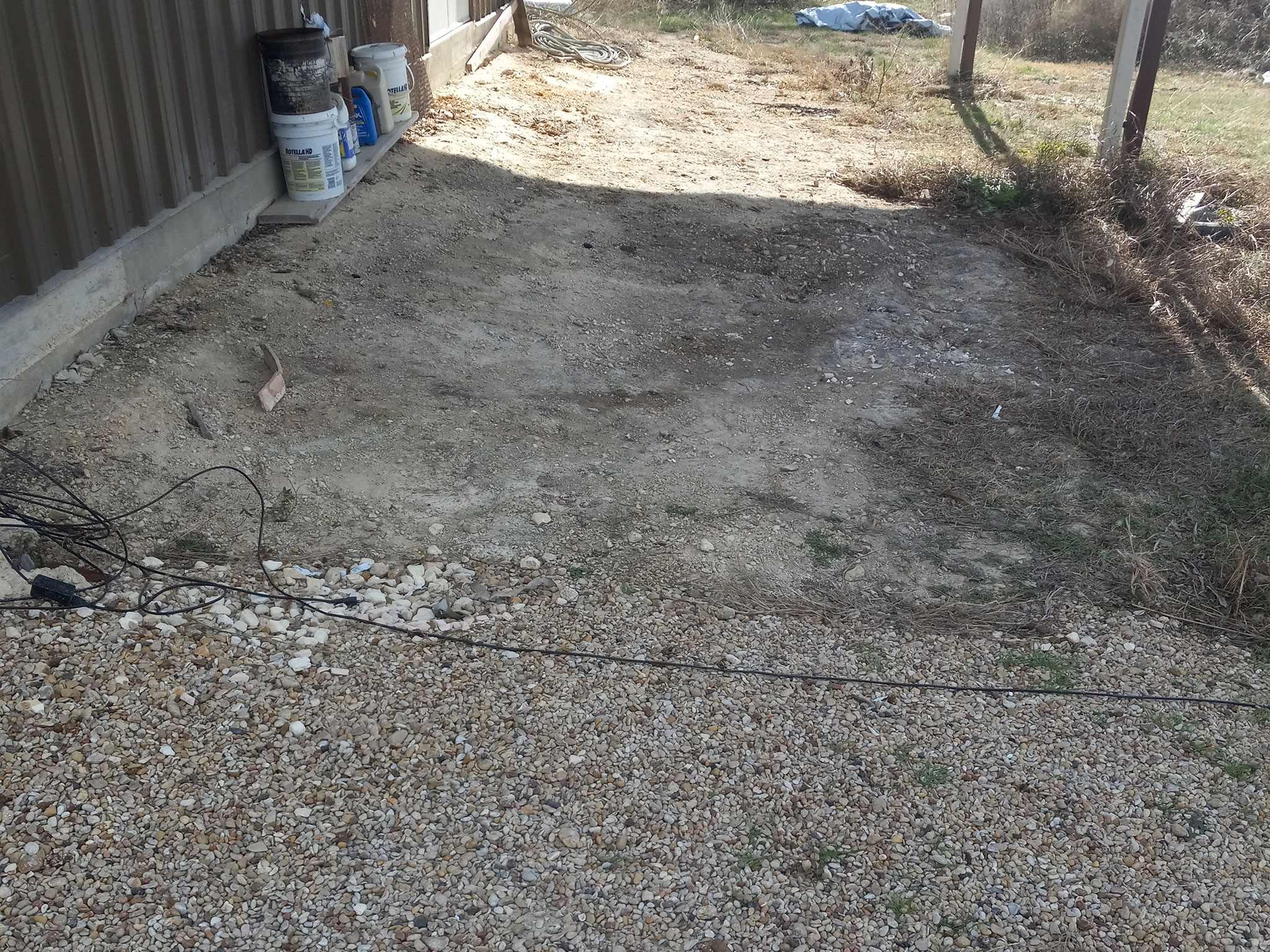 Gravel driveway next to corrugated metal building.