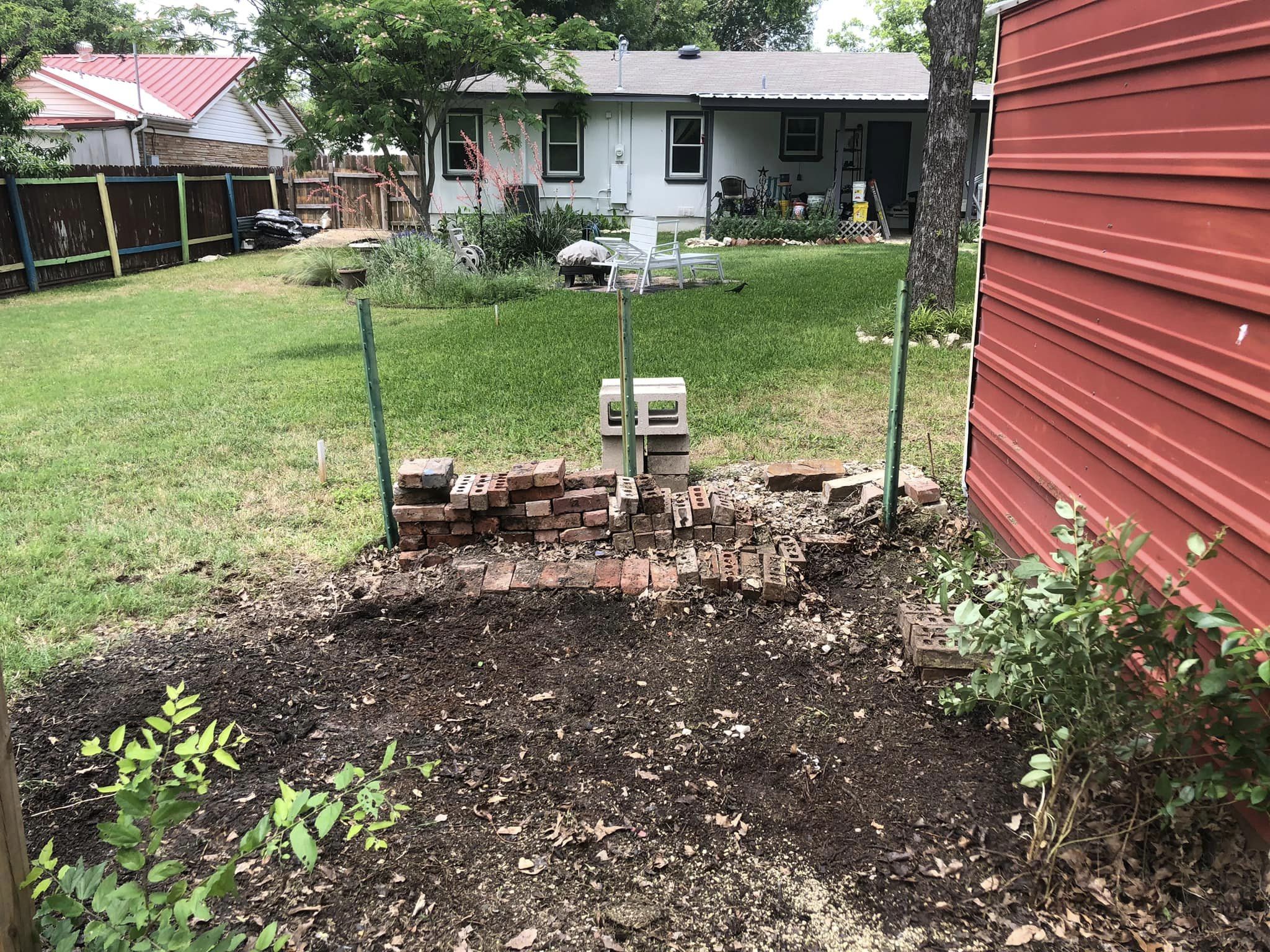 Backyard garden plot with bricks, green grass, and house in the background.