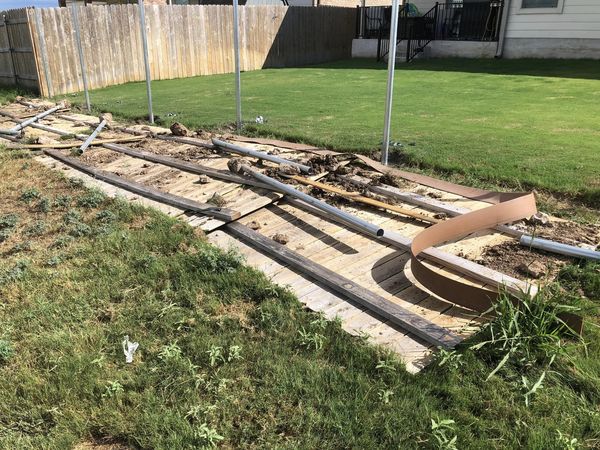 Deconstructed wooden deck with metal poles and fence in the background.