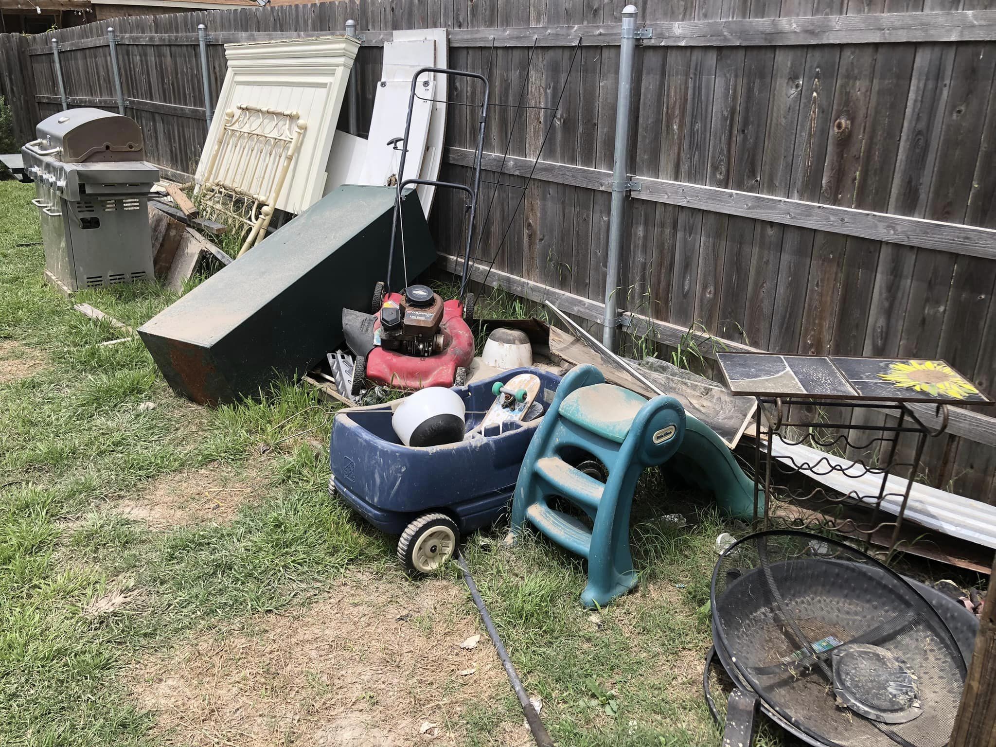 Backyard cluttered with debris, including lawnmower, grill, slide, and fence.